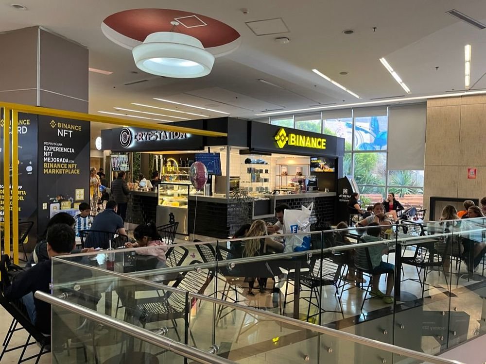 Patio gastronómico operado por DAF en el shopping, con la barra de Crypstation y el local de Binance al fondo y las mesas ocupadas
