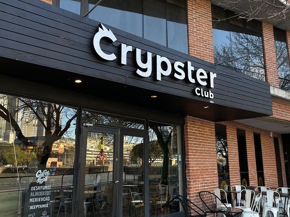 Fachada de Crypster Club con el cartel sobre el frente de ladrillo y la cartelera de desayunos, almuerzos y meriendas